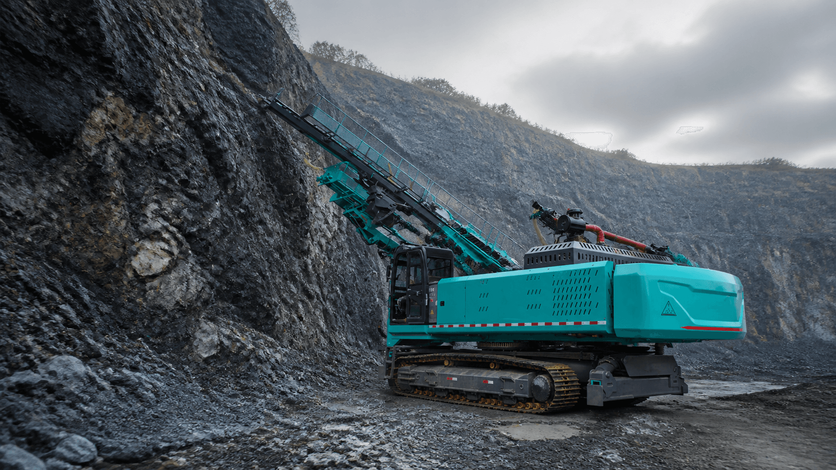 Teal crawler slope drilling rig working beside a quarry rock face